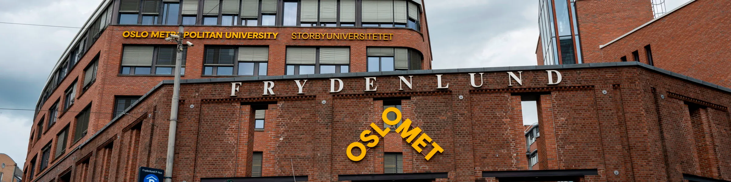 Bilde av inngangspartiet til campus Pilestredet med OsloMet navn og logo synlig og Frydenlund over OsloMet sin logo