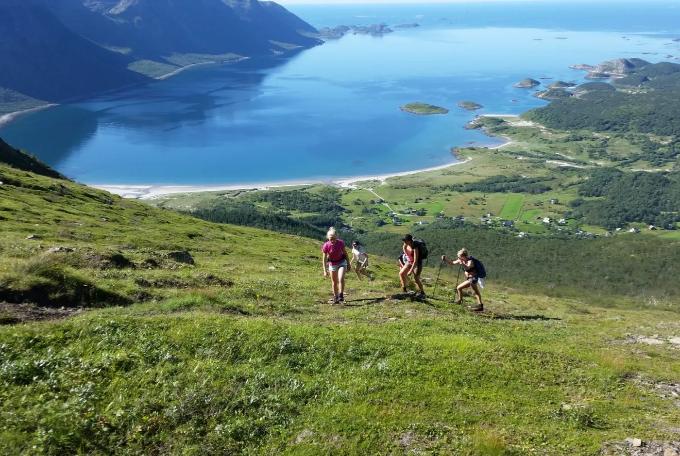 Tre damer på tur i fjellet med gårder og havet bak